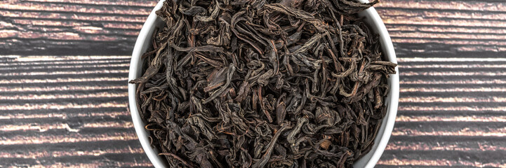 Dried tea is poured into a ceramic cup on a wooden plank table. View from above.