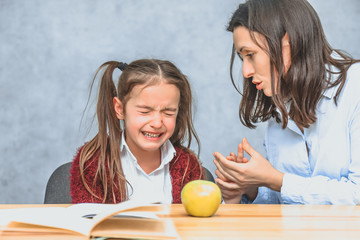 Mom talking to her baby. During this on a gray background. The girl cries, mom stroking her hand and talking to her daughter. Gray background. On the desk of the book and a green apple.