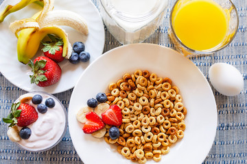 Flat lay of a bowl of oat cereal with bananas, strawberries, and blueberries.  Additional yogurt,...