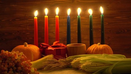 Kwanzaa festive concept with burning seven candles red, black and green decorated corns, grapes, bananas, gift boxes, pumpkin, bowl and fruits - Powered by Adobe
