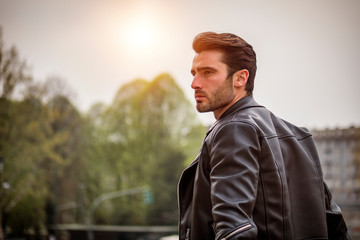 One handsome young man in urban setting in modern city, standing, wearing black leather jacket and...