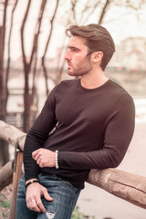 One handsome young man in urban setting in modern city, standing, wearing black leather jacket and jeans, looking away