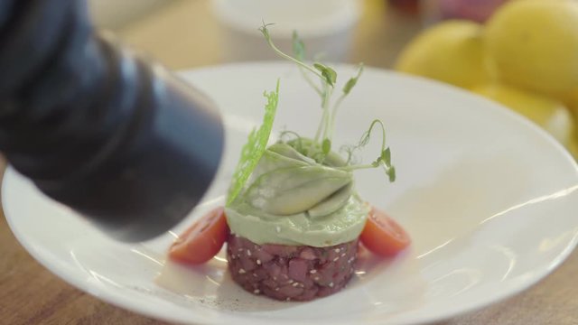 White big plate with amazing decoration of a dish. Round shape of small cutted tuna fish, on top green sause and greens. Beautiful decoration.