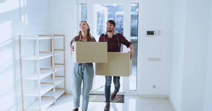 Smiling and feeling excited a new married couple moving to a new spacious house they have a moving day carrying the boxes into the house