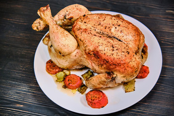 Fried chicken with golden crust on dark wooden background. Big whole grilled chicken on a plate. Festive dinner with meat bird.