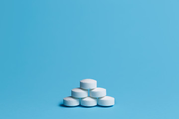 Heap of white pills on blue background. Medical, pharmacy and healthcare concept.