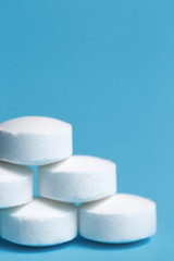 Close-up photo of a heap of white pills on blue background. Medical, pharmacy and healthcare concept.