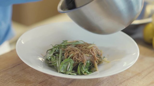 Hand of chef in black latex glove put a salad with glass noodles and aragula