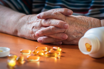 Old female hands and fish oil pills on table