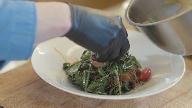 Close up hand of chef in black latex glove put a salad with glass noodles and aragula