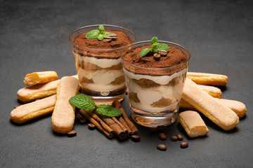 Classic tiramisu dessert in a glass and savoiardi cookies on dark concrete background