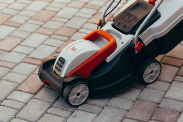 new electric lawn mower on the tile near the garden.