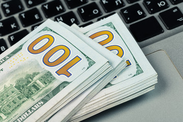 Closeup view of one hundred dollar banknotes lying on the laptop keyboard