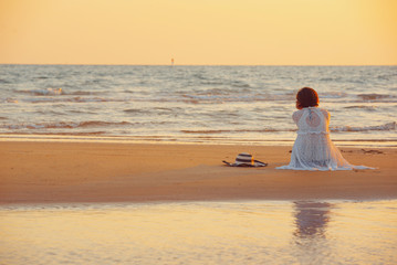 Fototapeta premium A young woman stands on the beach during a sunset, summer vacation.