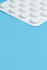 Close-up vertical photo white blister of pills on blue background. Medical, pharmacy and healthcare concept.