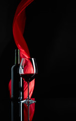 Wineglass and bottle of red wine on a black reflective background.