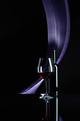 Wineglass and bottle of red wine on a black reflective background.