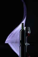 Wineglass and bottle of red wine on a black reflective background.