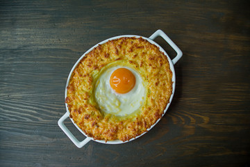 Potato casserole with bolognese. Baked potato casserole with egg and grated cheese in a ceramic oval baking sheet. Wooden dark background.