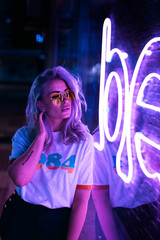 Lovely blonde woman with glasses on the street with neon background