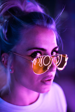 Lovely blonde woman with glasses on the street with neon background