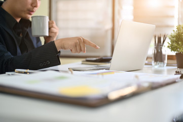 Cropped shot businessman using laptop and holding coffee mug on workplace.