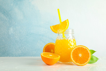 Glass jar with fresh orange juice and tubule, oranges on white table against color background, space for text. Fresh natural drink
