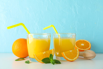 Flat lay composition with fresh orange juices, wooden juicer, mint, oranges and wooden juicer on white table against color background, space for text. Fresh natural drink and fruits