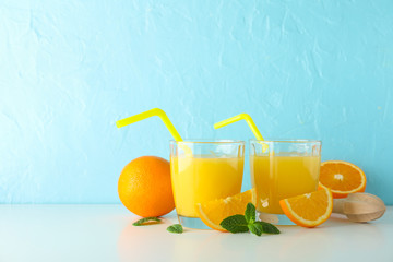 Flat lay composition with fresh orange juices, wooden juicer, mint, oranges and wooden juicer on white table against color background, space for text. Fresh natural drink and fruits