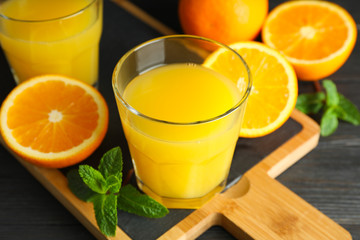 Cutting board with orange juice, mint and oranges on wooden table against black background, closeup. Fresh drinks and fruits