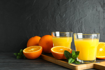 Fototapeta na wymiar Cutting board with orange juice, mint and oranges on wooden table against black background, space for text. Fresh drinks and fruits