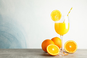 Glass with fresh orange juice and tubule, oranges on grey table against color background, space for...