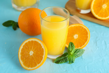 Composition with fresh orange juice in glass, mint, wooden juicer and oranges on color background, closeup. Fresh natural drink