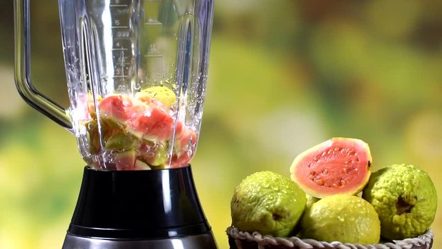 Water pouring in a blender with red guava. Tree unfocused background . Preparing juice. Slow motion.
