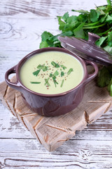 Green cream soup in a ceramic pan against the white wooden background