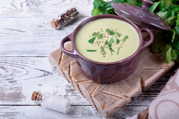 Green cream soup in a ceramic pan against the white wooden background
