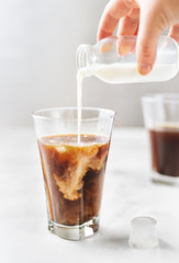 Iced coffee with pouring milk in glass on white background