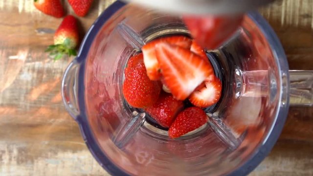 Strawberry fruit falling into the blender in slow motion. Top view.