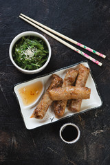 Plate with vietnamese fried spring rolls or nems, dips and seaweed salad. Flatlay on a dark brown stone background
