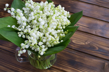 Bouquet of lily of the valley  in the glass jug on the brown wooden  background.Top view.Spring flowers concept.