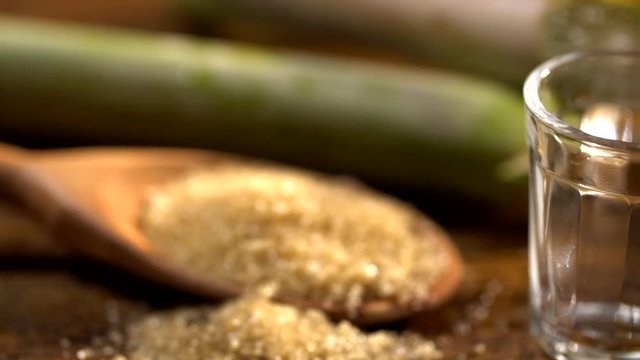 Brazilian gold cachaca pouring in glass cup. Sugar Cane Derivatives. Sugar and sugarcane on old wood background.