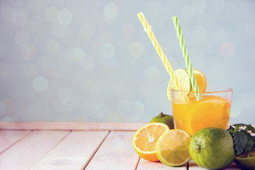 A cool drink of citrus. Orange  lemonade in a transparent glass with a straw, next to it are oranges and limes, fresh mint. Copy space.