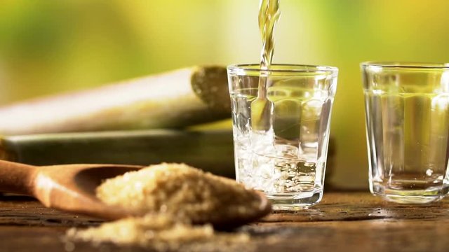 Brazilian gold cachaca pouring in glass cup. Sugar Cane Derivatives. Sugar and sugarcane on old wood background.