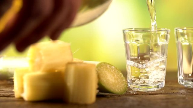 Brazilian gold cachaca pouring in glass cup. Sugar Cane Derivatives. Sugar and sugarcane on old wood background.