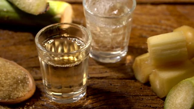 Brazilian gold cachaca pouring in glass cup. Sugar Cane Derivatives. Sugar and sugarcane on old wood background.