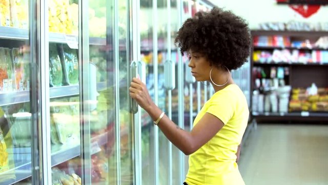 Pretty African woman taking product on fridge at supermarket
