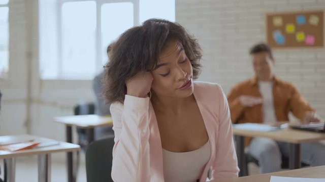 tired sleepy woman falls asleep at a lecture. An exotic-looking girl is yawning and blinking slowly. Group of students in the background. 4K