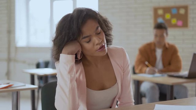 tired sleepy woman sleeping in a lecture. dark-skinned girl is yawning. Group of students in the background .4k
