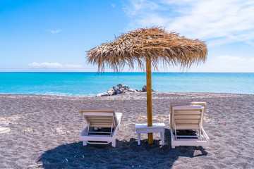 Empty deck chairs and umbrella on the black sand beach in Perissa, Santorini, Greece