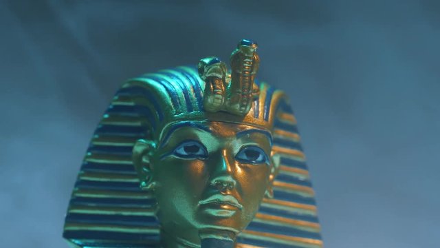 Dramatic shot of a pharaoh mask figure appearing in smoke.